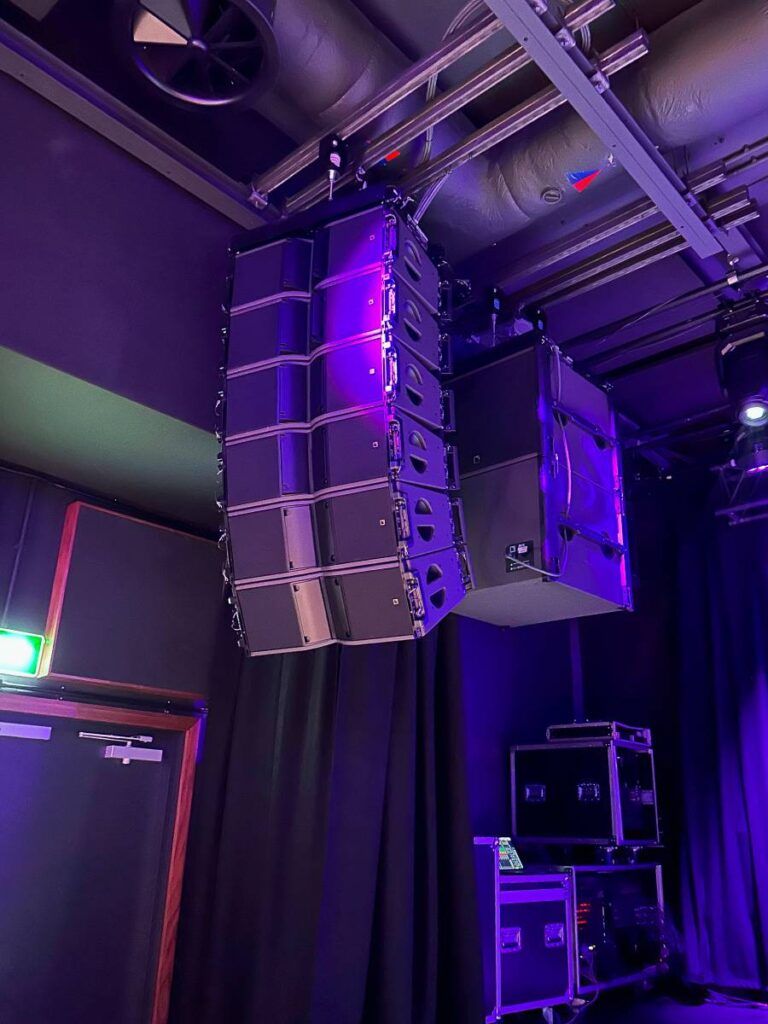 Four flown L-Acoustics SB18 subwoofers are flowing behind the main hangs due to the venue's height restrictions