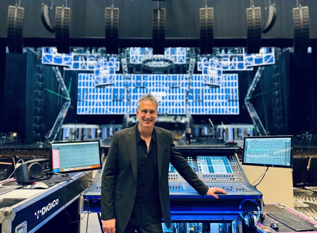 FOH engineer Caram Costanzo standing at the show’s DiGiCo Quantum338 mixing console with Resorts World Theatre’s L-Acoustics K2 and Kara Immersive Sound arrays seen in the upper background